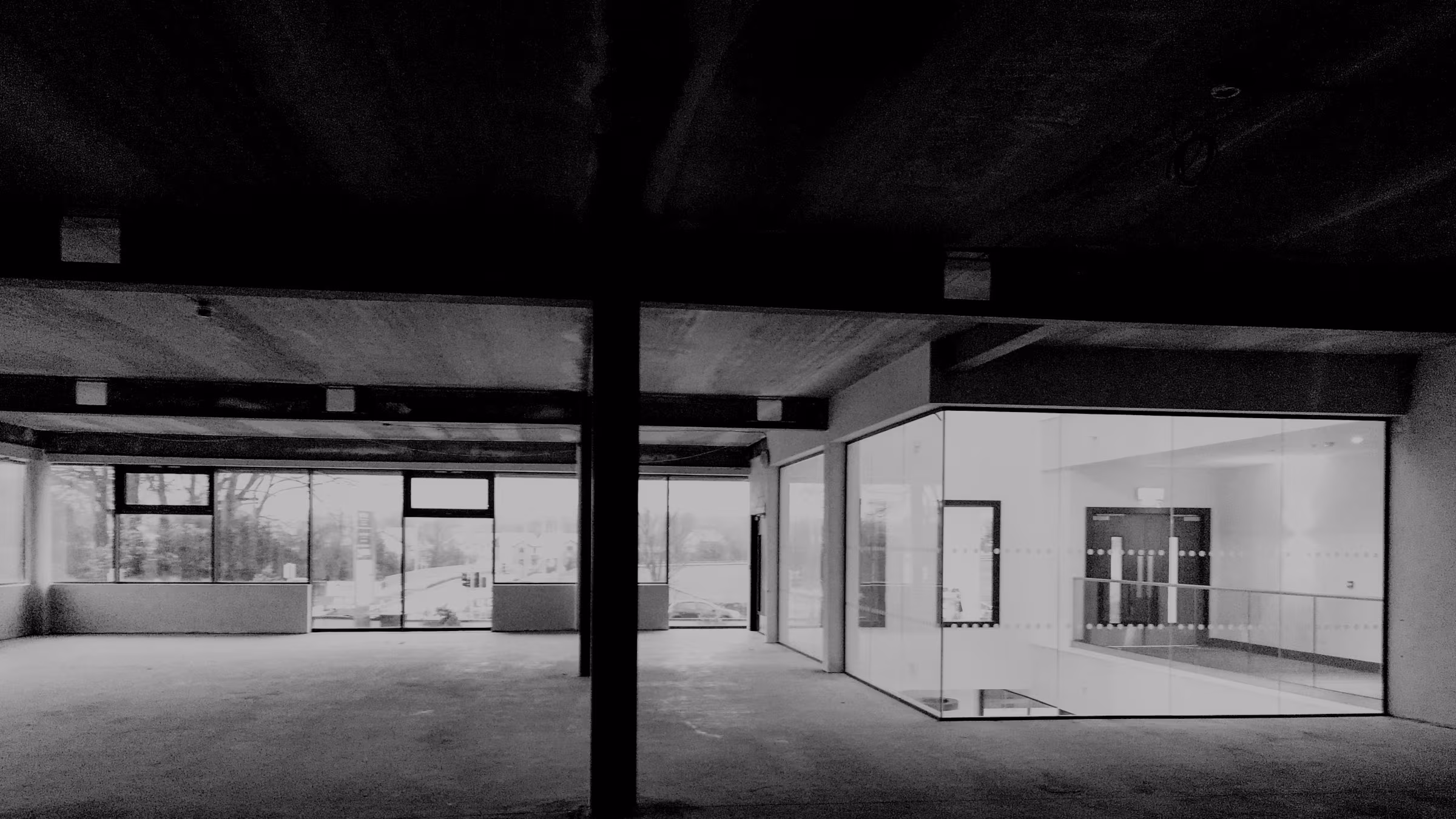 Open-plan commercial interior with full-height glass walls and exposed concrete beams