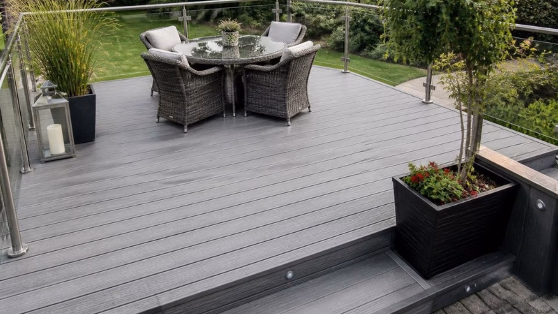 Grey composite decking with a glass balustrade and garden furniture