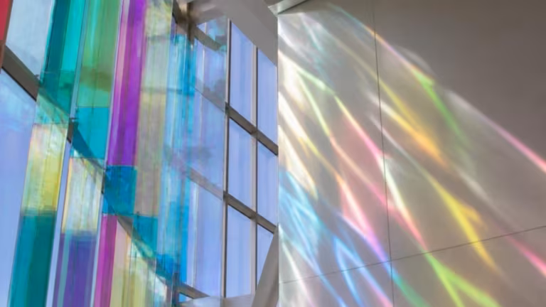 Dichroic glass panels casting coloured light across a white wall